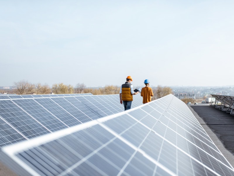 Zwei Menschen stehen neben Solarpanelen auf dem Dach einer Industriehalle