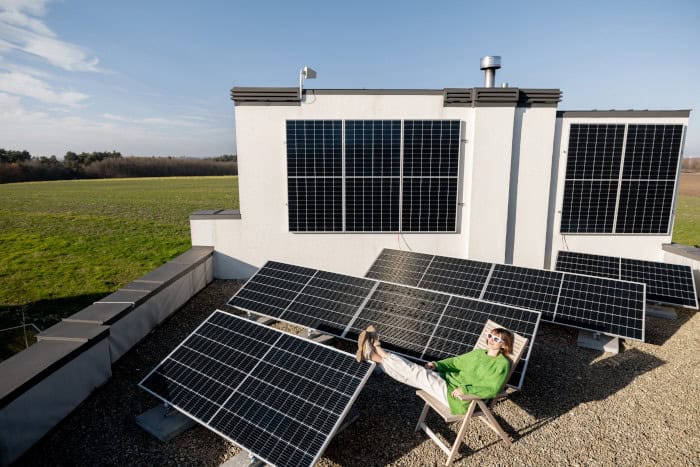Junge Frau sitzt entspannt auf einem Dach zwischen Solarmodulen